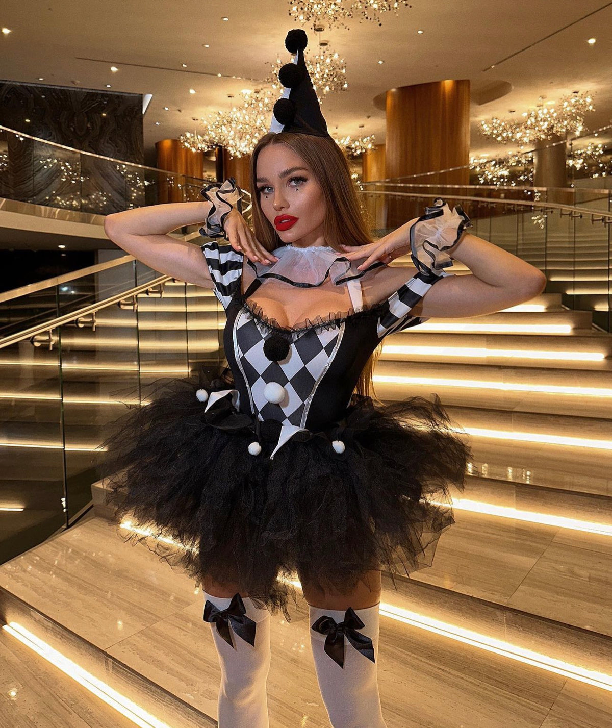 Woman in a circus clown costume with a black and white checkered pattern, including a bodysuit, ruffles, and a clown hat headband.
