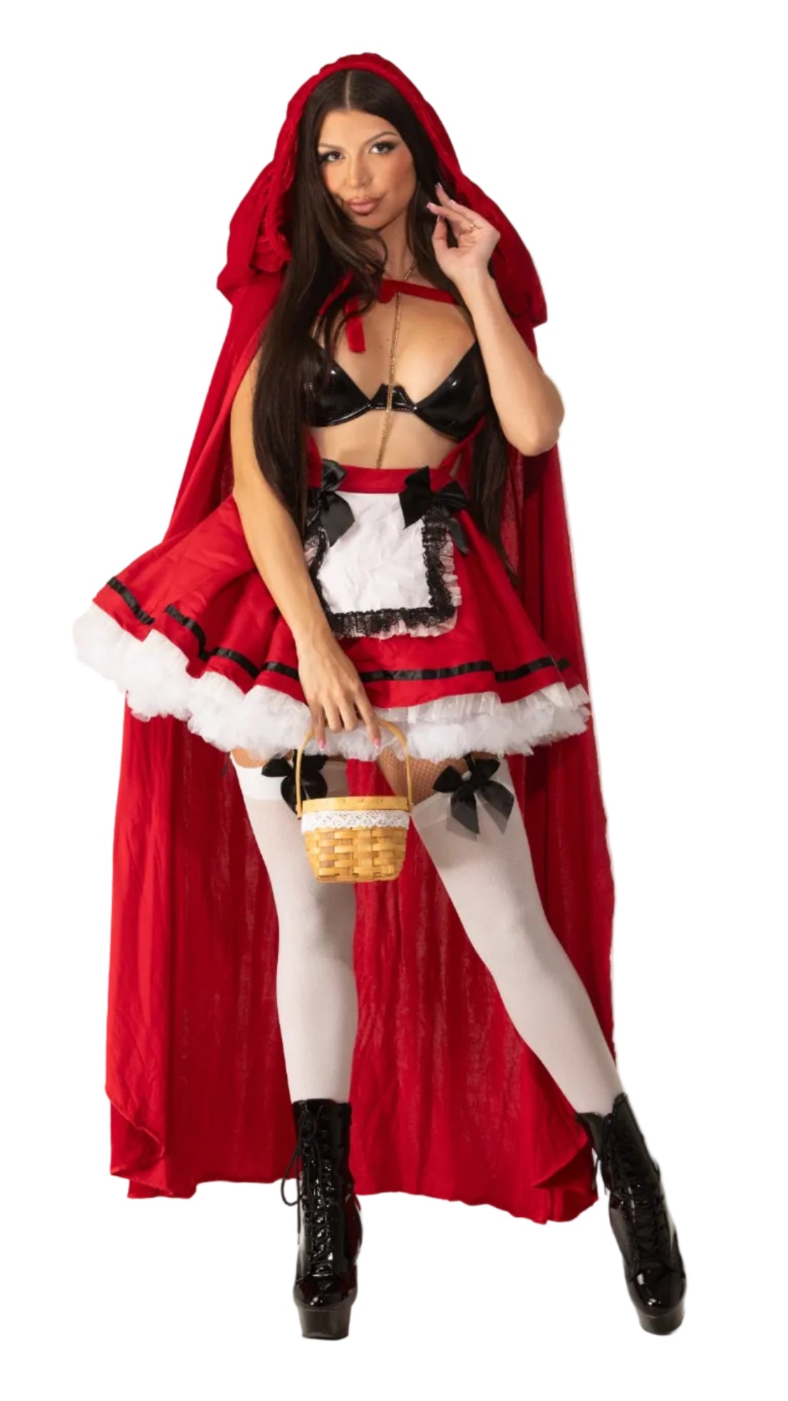 A woman modeling a Little Red Riding Hood costume against a plain white studio background. The costume includes a red hooded cape, a black-and-white apron-style top with red trim, white tights, black lace-up boots, and a small woven basket.